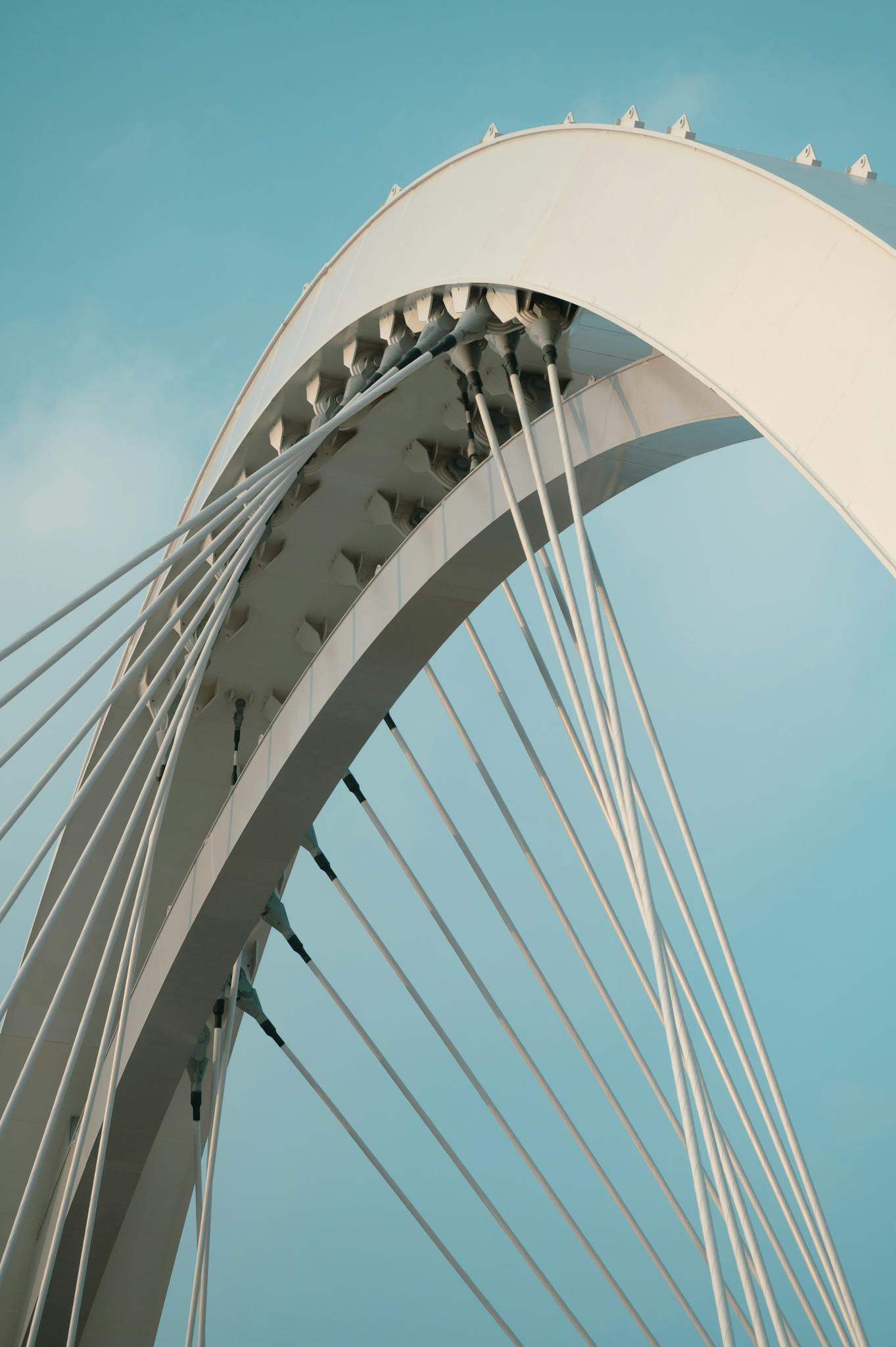Close-up of a modern suspension bridge with geometric arches under a blue sky.