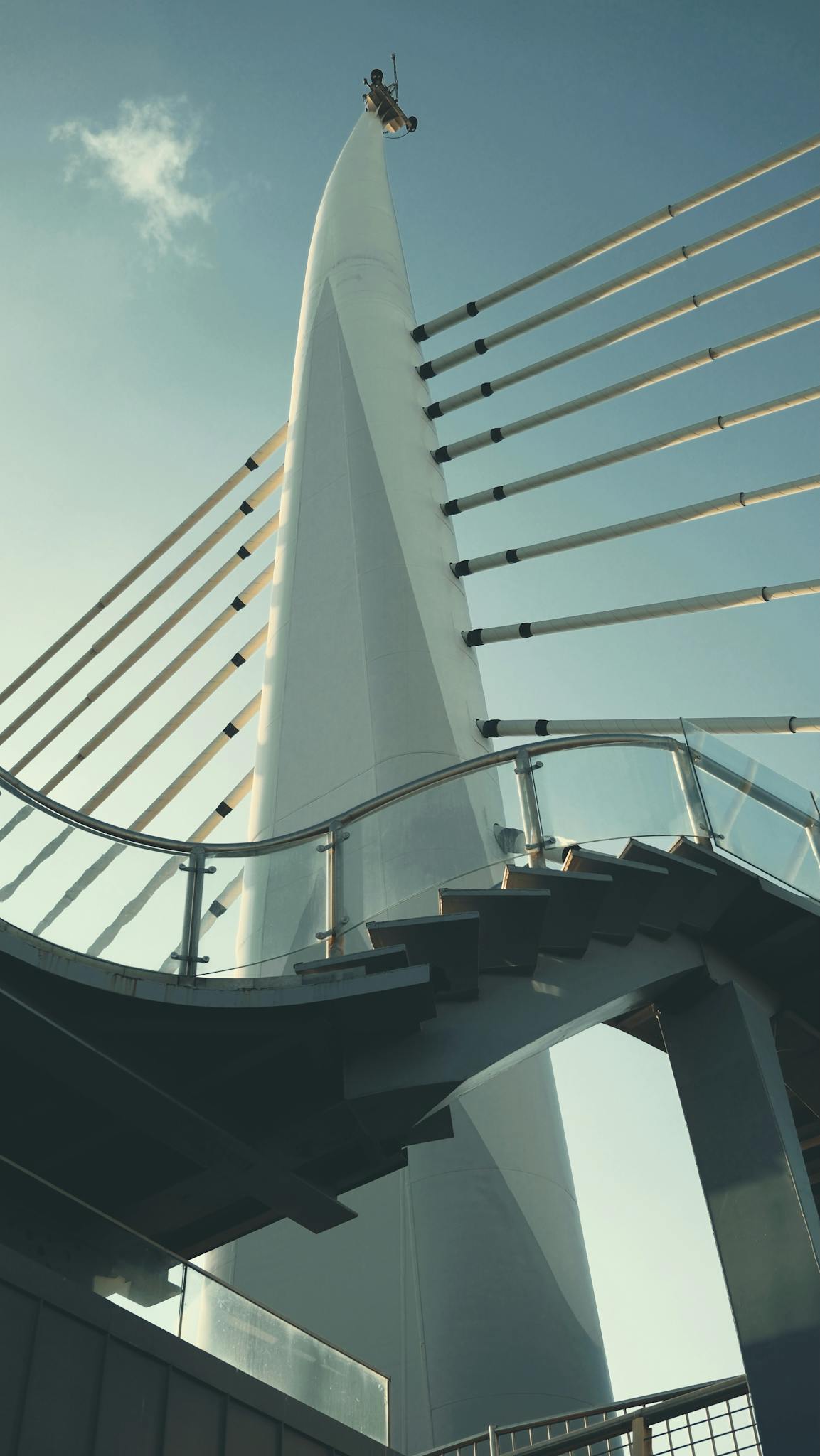 Dynamic view of a modern bridge tower with distinctive cables and stairway.